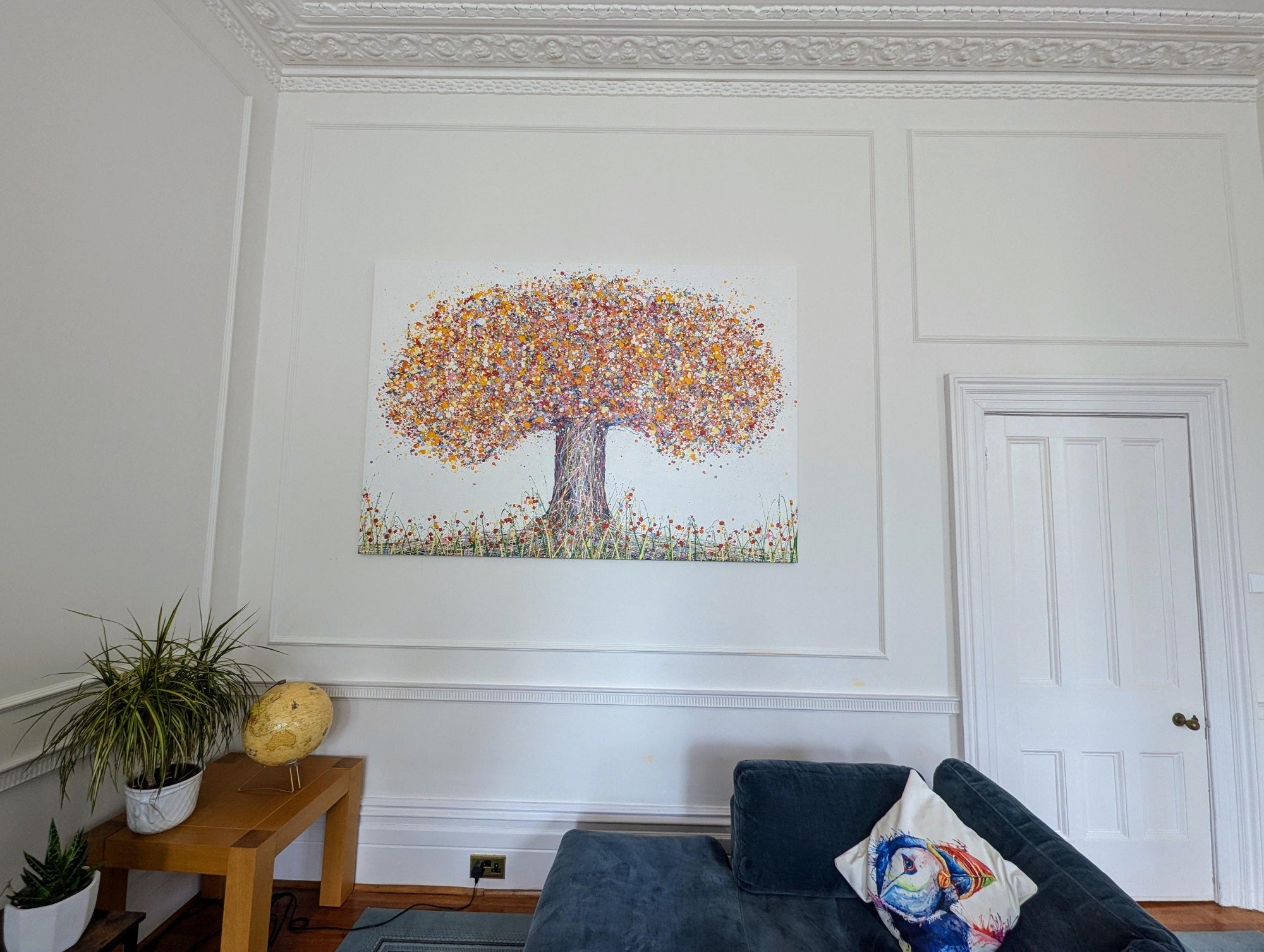 Living room with a colorful tree painting on the wall, a blue sofa, and a small table with plants.