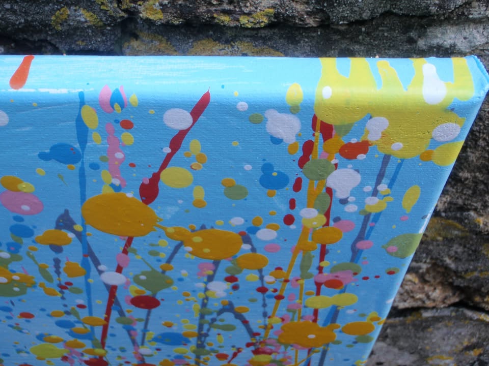 A colourful abstract landscape painting depicting a field of tall grass under a blue sky, with splatters and drips of yellow, red, orange, blue, pink, and green paint throughout. Hand-painted on to a large 101.5 by 81 cm stretched canvas - detail