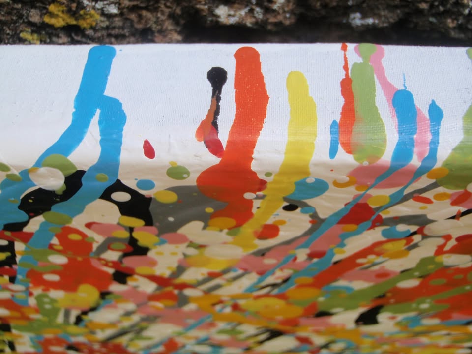 Abstract radial burst painting with dense splatters and streaks of yellow, orange, white, blue, pink, red, and green radiating outward from a bright central area, on 80 by 60 cm canvas - detail