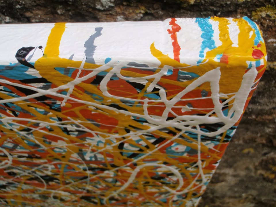 An abstract painting filled with dense, energetic splatters and drips in orange, yellow, white, black, and light blue, hand-painted on to a large framed wooden panel - detail