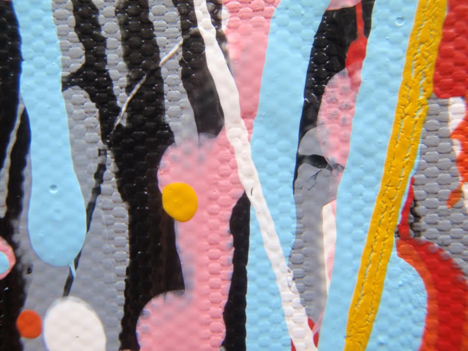 Abstract wall art featuring the word 'JOY' formed by dripping, splattered paint in multiple colours including red, blue, yellow, black, and white on a light background - detail