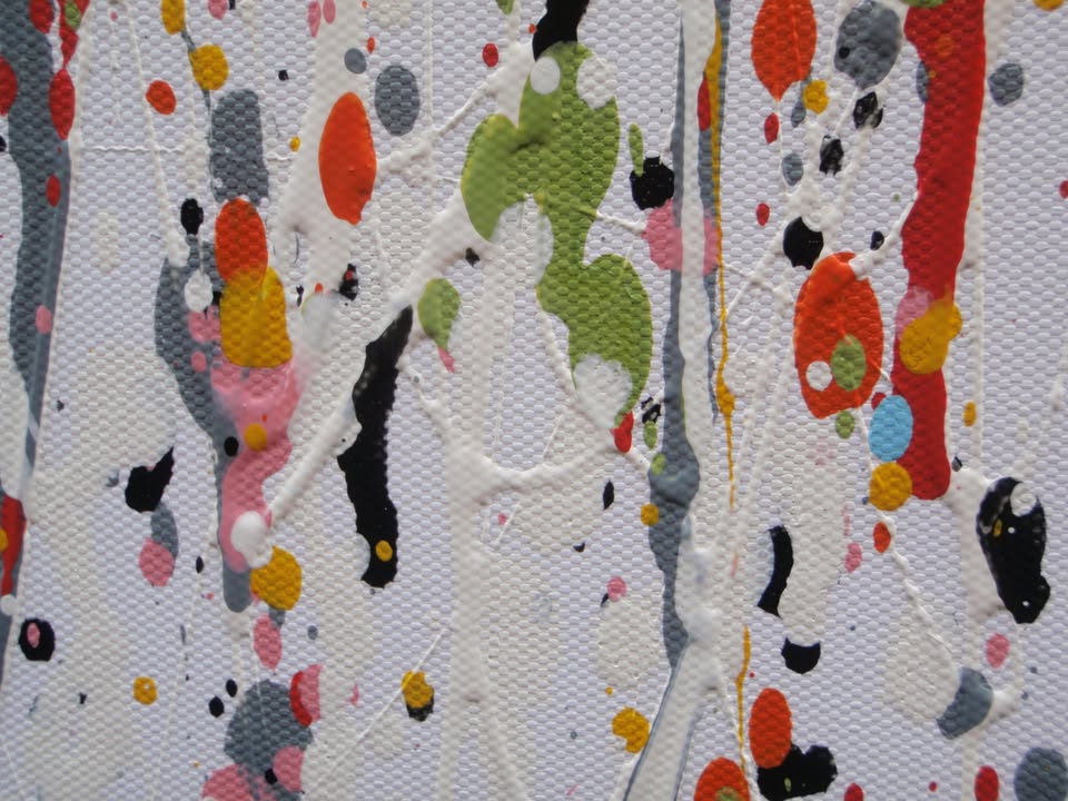 Abstract wall art featuring the word 'JOY' formed by dripping, splattered paint in multiple colours including red, blue, yellow, black, and white on a light background - detail